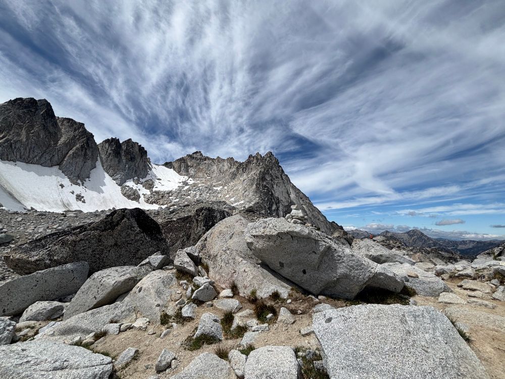 Jagged granite peaks with snow-covered flanks rise sharply from an alpine bench. The large granite boulders on the foreground are bleached white.