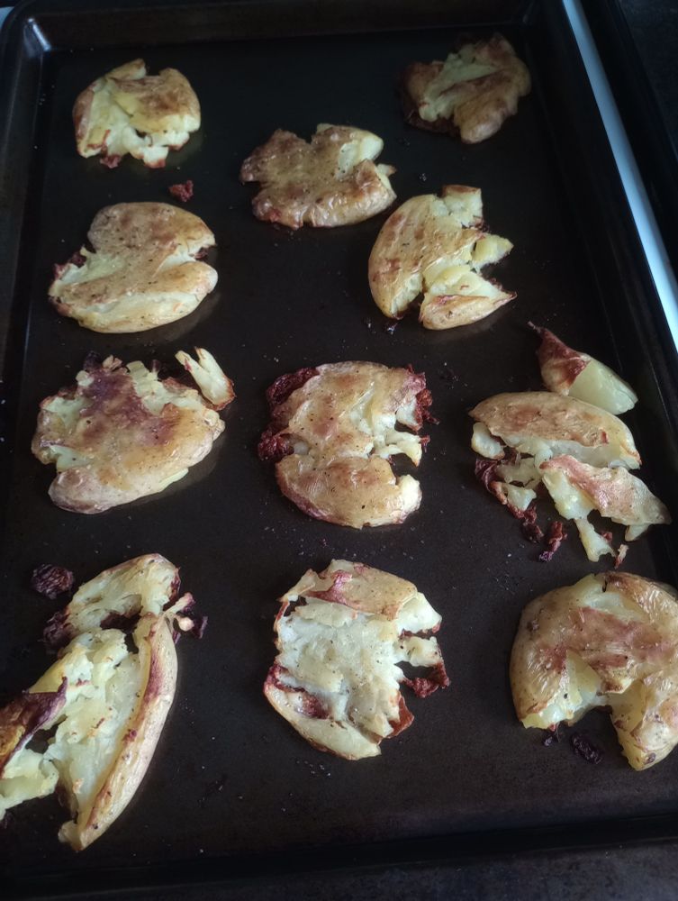 A photo of small potatoes that have been smashed and then roasted, sitting on a sheet pan.  The edges are crisped and browned.