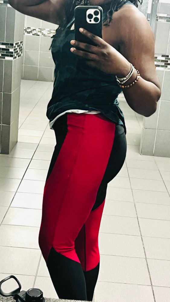 Sheron in a tank top and black and pink puma leggings posing in gym locker room mirror