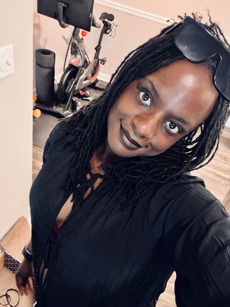 Sheron posing in front of camera. She has sunglasses on the top of her head and she is smiling at the camera.