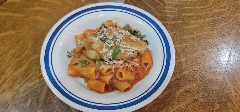 A bowl of rigatoni and sauce with breaded chicken.