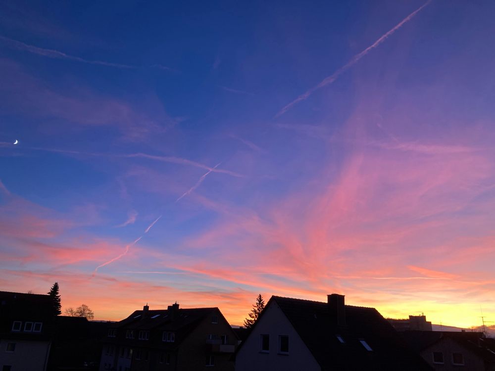 Sonnenuntergang mit Häusern im Vordergrund. Der Himmel ist noch blau und die Wolken sind Orange von der untergegangenen Sonne