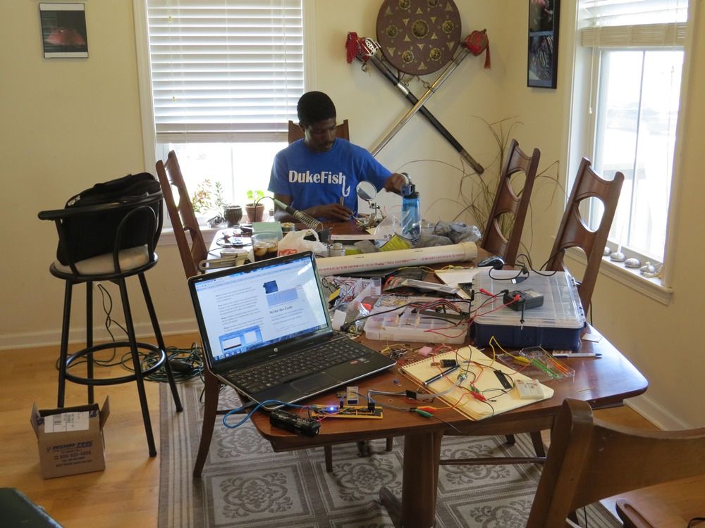 Kersey working at a soldering station surrounded by Andrew's absolute nonsense piles of electronics. 