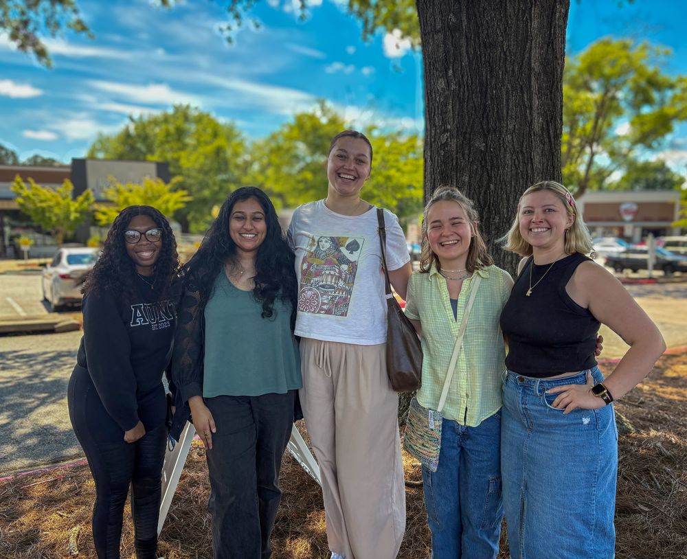 Photo of 5 recent graduates smiling outside in front of a tree.