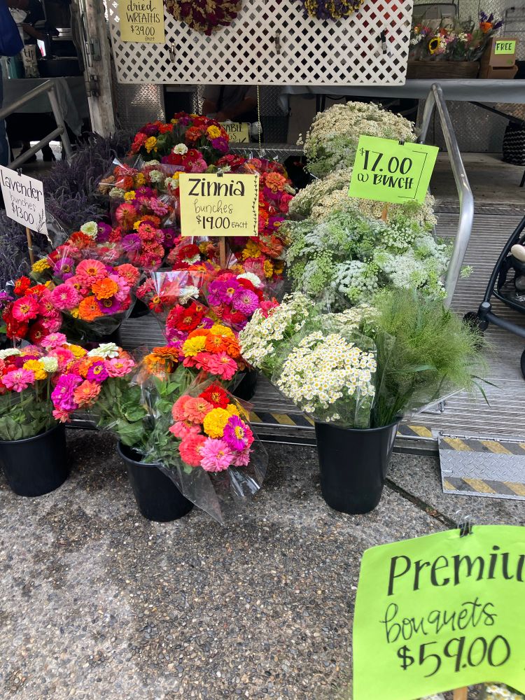 Pink, orange and yellow zinnias and white babys breath, in outdoor bins at a farmers market.