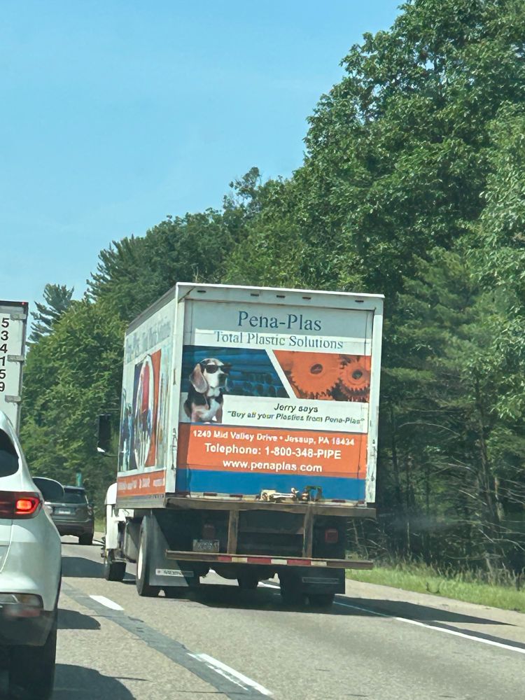 Large truck stuck in traffic. Ad for local plastic company on the back. Mascot is a beagle wearing sunglasses named Jerry. 