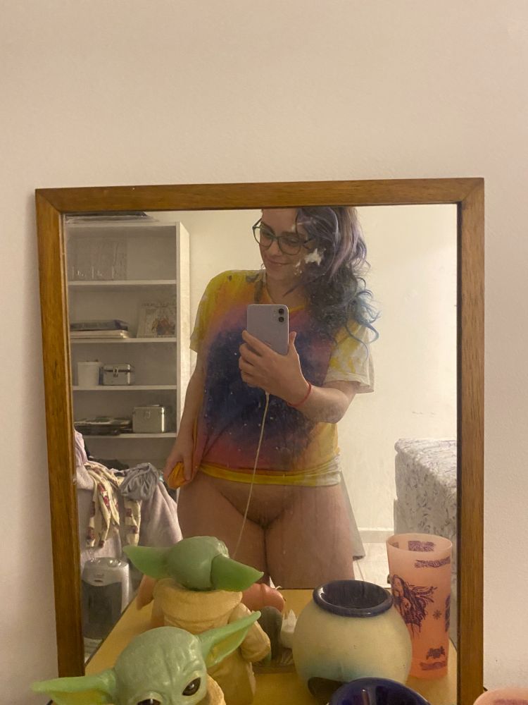 A photo of me in the mirror! I'm only wearing a tie-dye shirt and my green glasses in front of a dresser with a Baby Yoda and some other random objects
