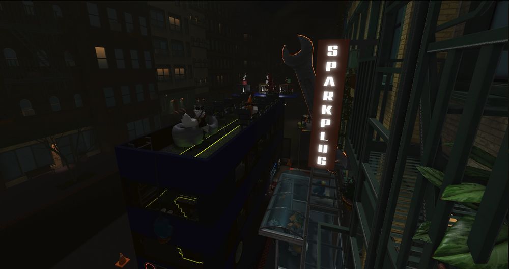 An outer view of the bus, parked next to the Sparkplug Cafe. Someone is sitting on a beanbag on the top floor. Most people are in the Cafe at this moment, though.