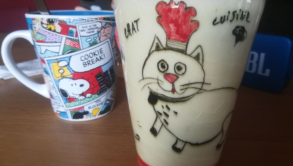 Deux tasses de thé, l'une avec un chat (à droite) l'autre des strips de peanuts