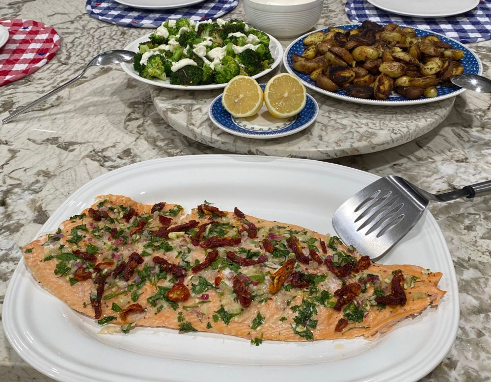 a platter of roasted salmon, a halved lemon, plate of broccoli, plate of potatoes 