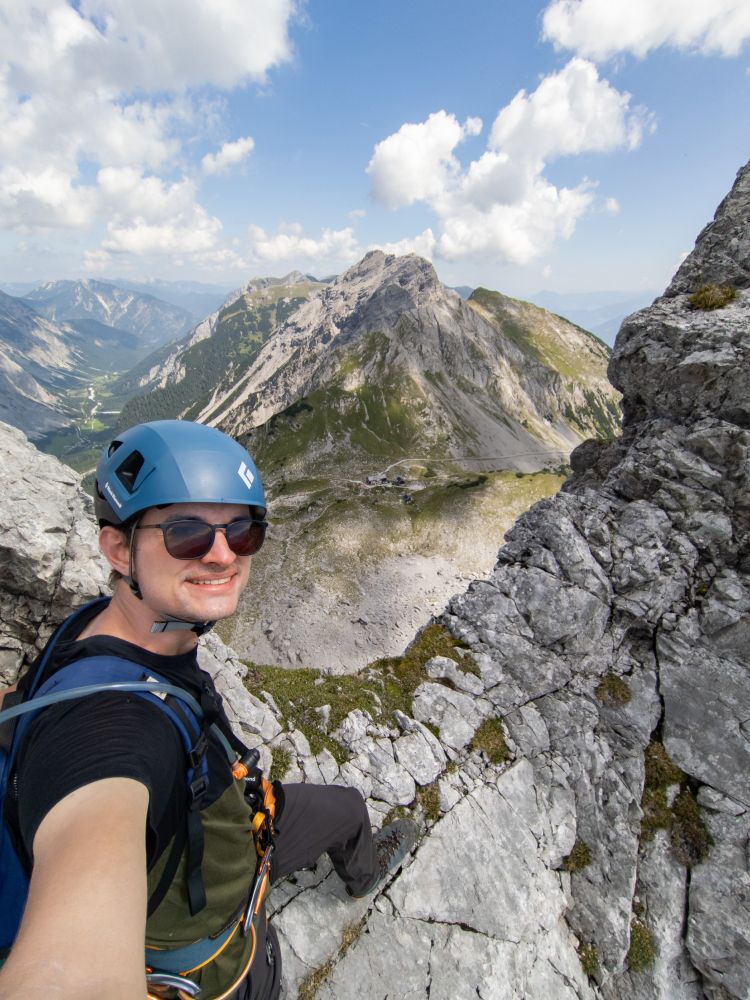 Selfie of me with climbing gear, standing on a mountain ridge overlooking the Lamsenjoch Hut. 
