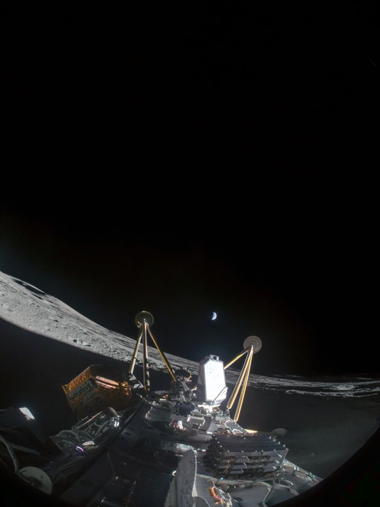 fisheye picture from the lunar surface taken by a camera attached to the top of the IM2 lander. The lander has fallen over on it's side and the legs point towards the small half lit earth in the far distance.
The crater partially lies in the shade, which covers most of the foreground. A small hill is visible on the horizon. 