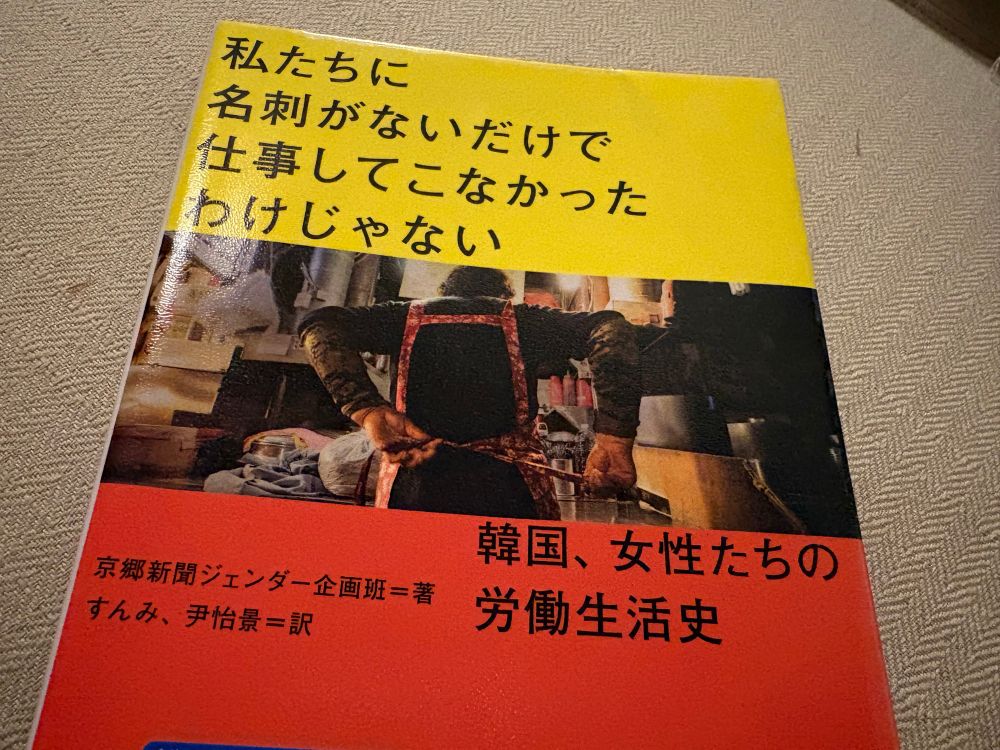 「私たちに名刺がないだけで仕事してこなかったわけじゃない」本の表紙。中央には台所のような場所で作業する人物の後ろ姿の写真があり、下部には「韓国、女性たちの労働生活史」と書かれている。タイトル部分は黄色、サブタイトル部は赤の印象的な表紙。