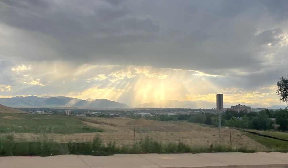 A picture of the sun making sunbeams through rainclouds over a mountain range 