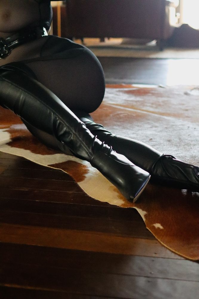 June is pictured with her face out of frame, lying on the earthen tones of a cow skin rug. Her body is clad in black mesh and her legs adorned with slick knee high black boots.