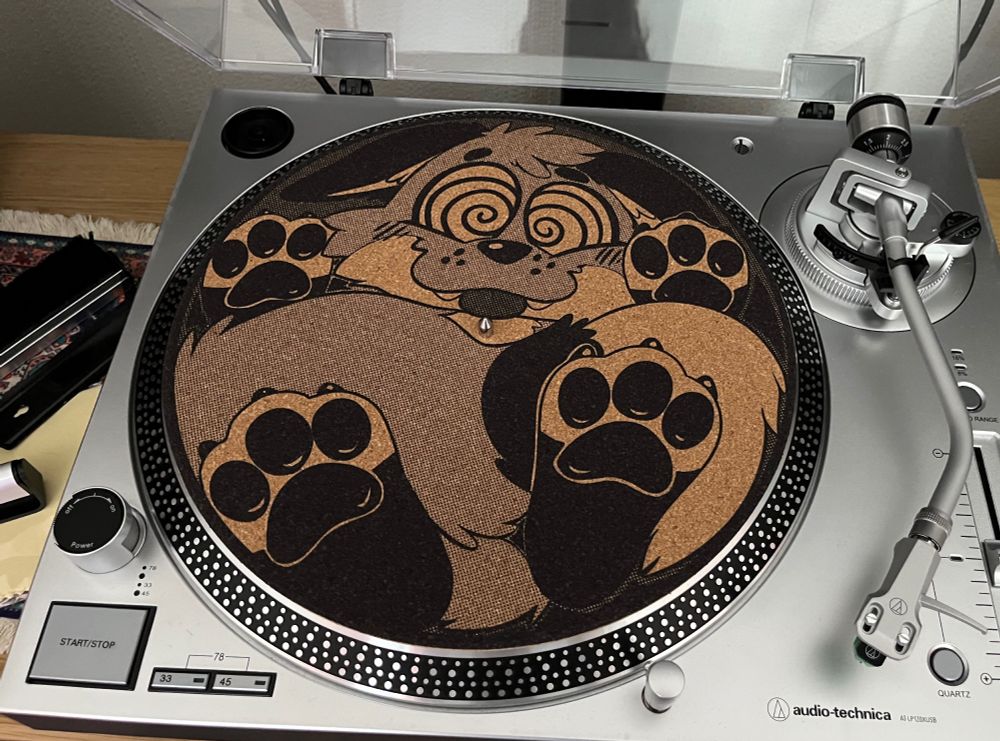 A cork slipmat on a turntable. A design of a toony fox flattened into a disc has been laser etched into it.