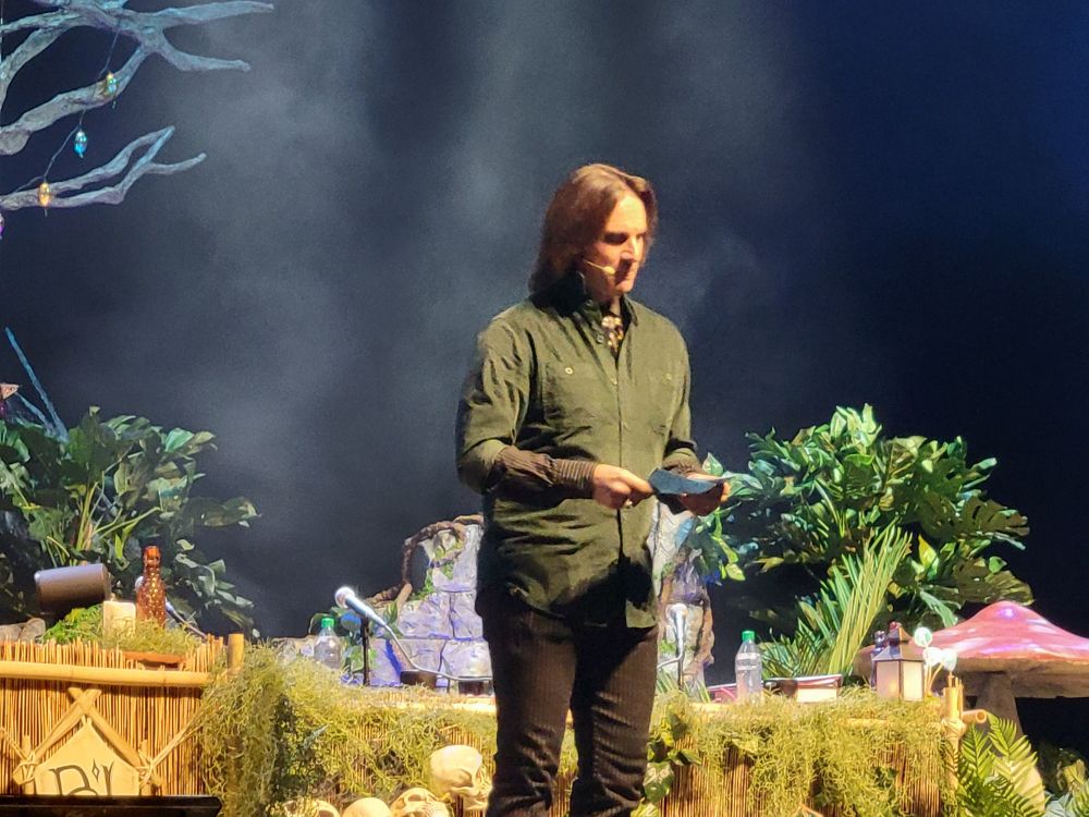 Matthew Mercer stands on stage before a live audience reading from a 3x5 card in his hand.