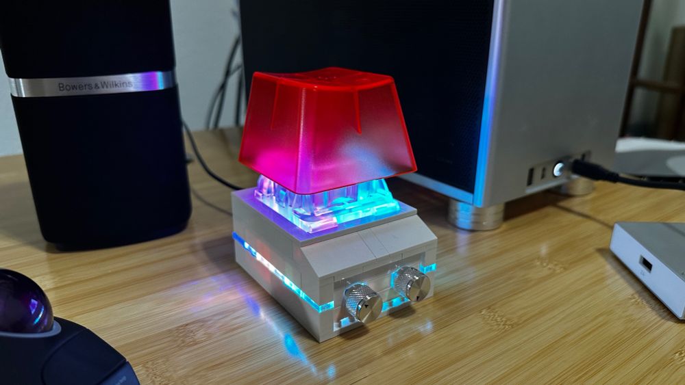 A photo of a macropod, if you can call it that, with one enormous mechanical key switch with an orange keycap, plus two rotary encoders. It has a case made of LEGO and you know it has RBG backlighting and underglow 