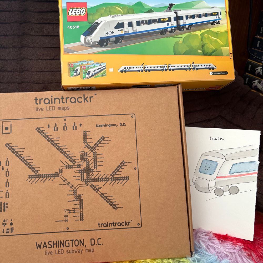 Three train-themed presents; a watercolor card, a LEGO high speed train set, and a traintrackr live LED subway map of the DC metro.
