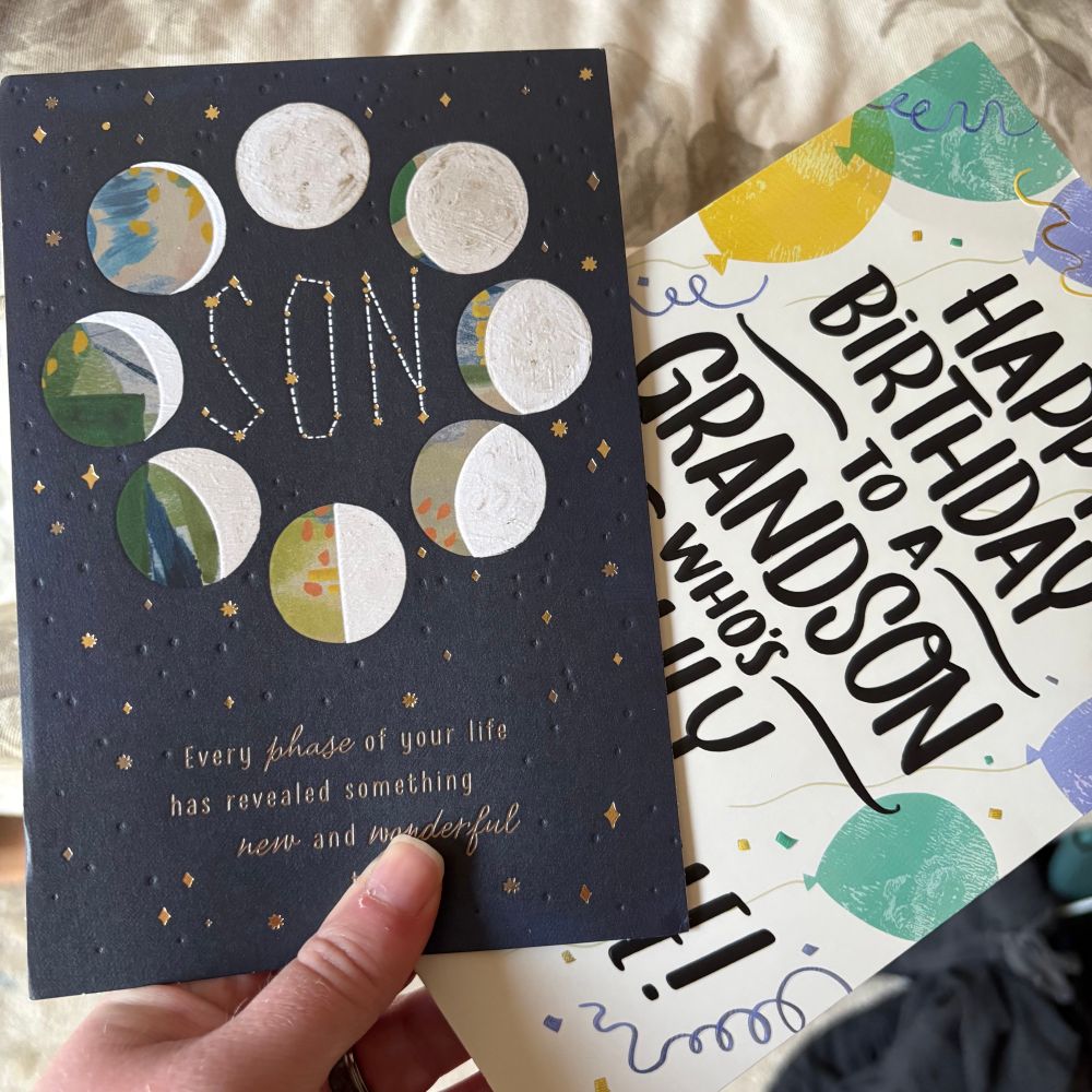 A white hand holding up two birthday cards, one for “son” and the other for “grandson”