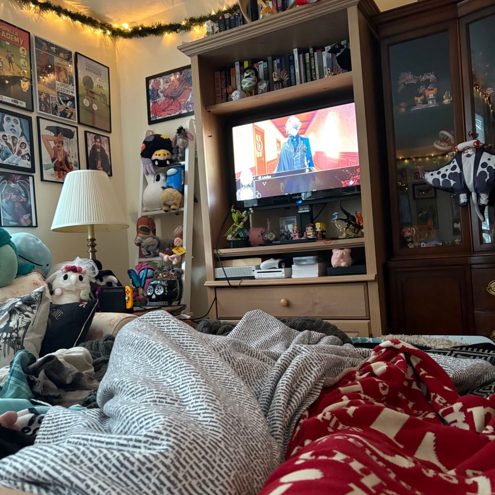 A picture of the corner of a living room, with three people on an air mattress on the floor, playing a video game. The living room is full of Legos, stuffed animals, and framed art prints. 