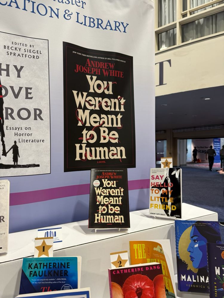 A book conference stand, featuring YOU WERENT MEANT TO BE HUMAN by Andrew Joseph White, with the cover of the book printed huge on the poster behind it.