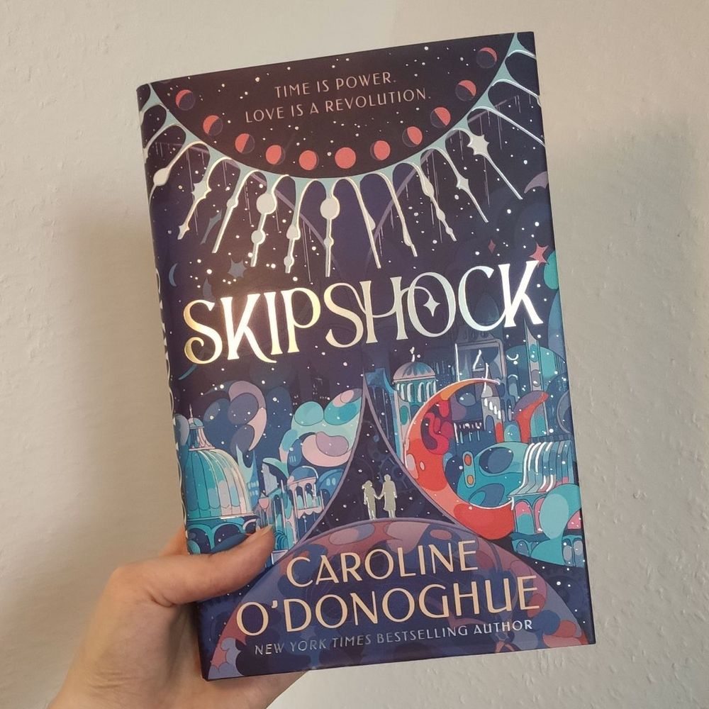 Hand holds a book. It is called Skipshock and has a very colourful cover.
