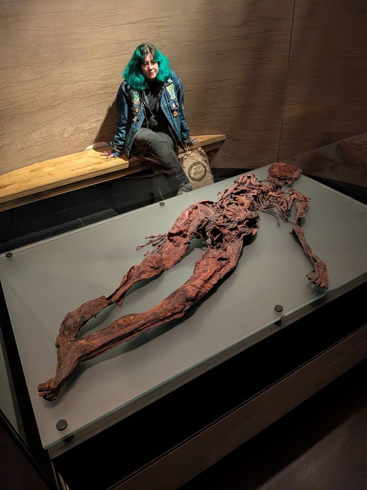 Woman with green hair stares adoringly at mummified bog body. 