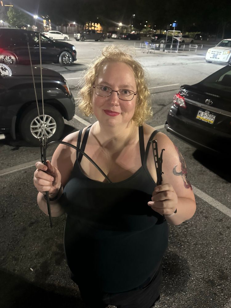 Photograph of a six foot tall blonde, holding two halves of a Metal Windshield wiper, having broken it with her bare hands. 