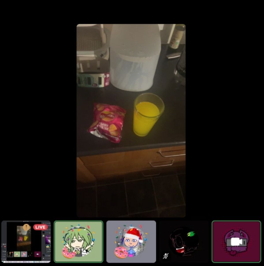 a picture of a discord vc with someones camera turned on, its showing a glass of orange juice and potato chips