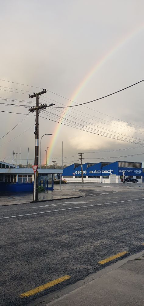 Portrait angle shot of a rainbow coming down behind pretty industrial looking streets and power lines