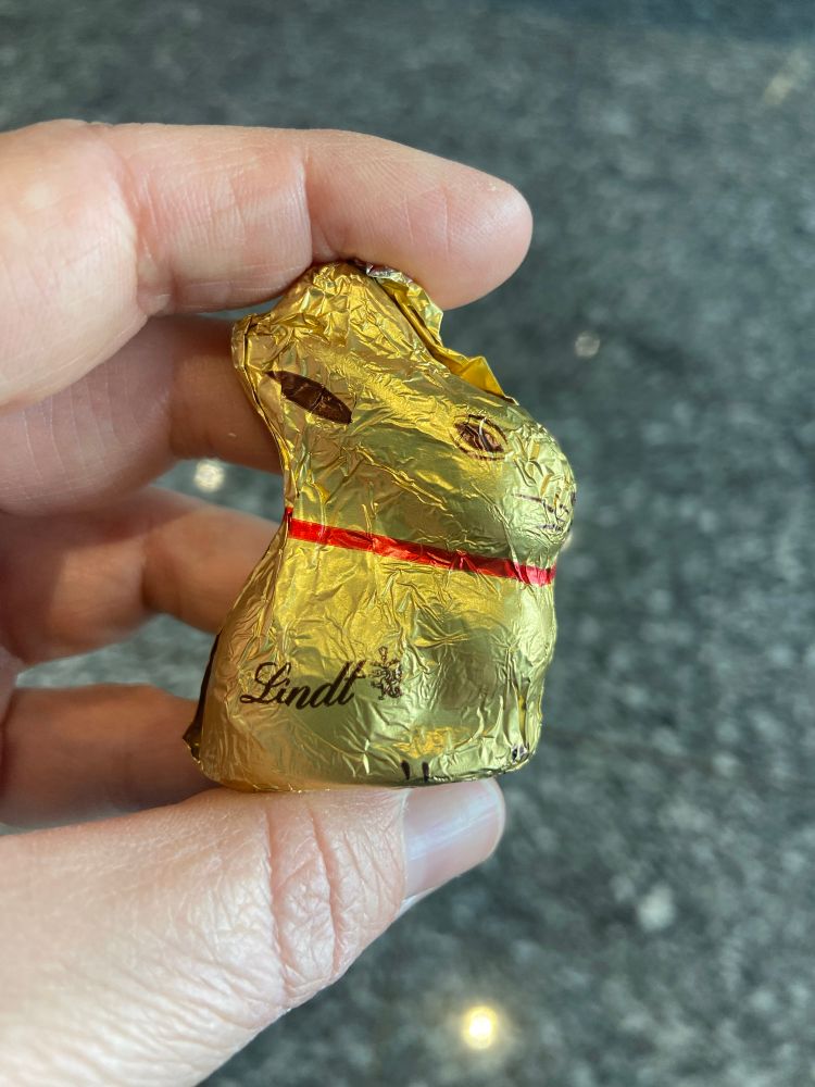 A mini Lindt chocolate bunny wrapped in gold foil with a red ribbon around his neck.