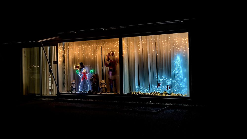 In dunkler Nacht leuchten zwei einzelne Schaufenster mit vielen kleinen Lichtern und verschiedenen Figuren, unter anderem ein Santa Claus. Die Beleuchtung der Dekoration ist insgesamt in sanft orangem und kaltweißem bis hellblauem Licht gehalten.