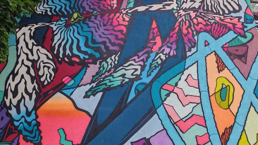 Ausschnitt eines wandgroßen Graffitis, das Bewegung ausdrücken will. Es handelt sich um rein abstrakte Kunst, mit dynamisch angeordneten, farbenfrohen Elementen.