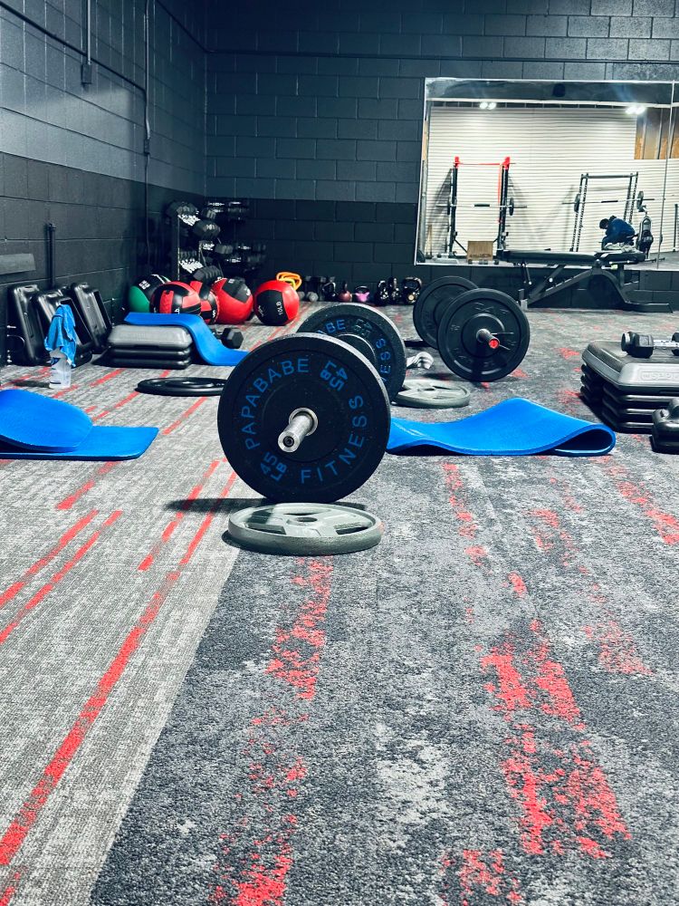 A strength training facility under construction with dark blue and black brick walls (one mirrored) and grey/red/white carpet.