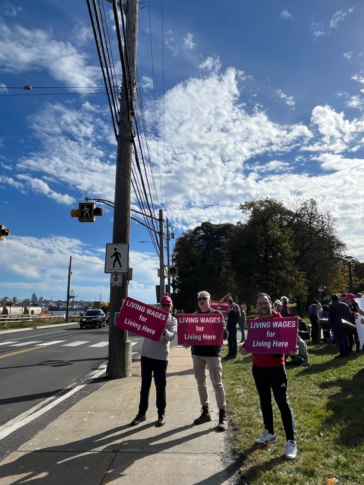 Workers striking, holding signs that read “living wages for living here”