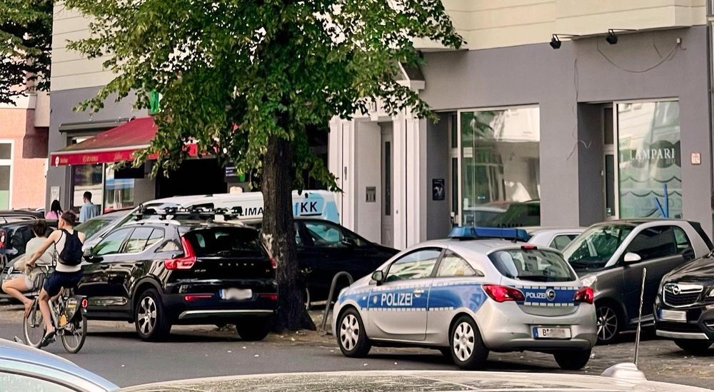 Straßenlaterne. Einige Autos vor einer Hausfassade, in zweiter Reihe steht ein Polizeiwagen.