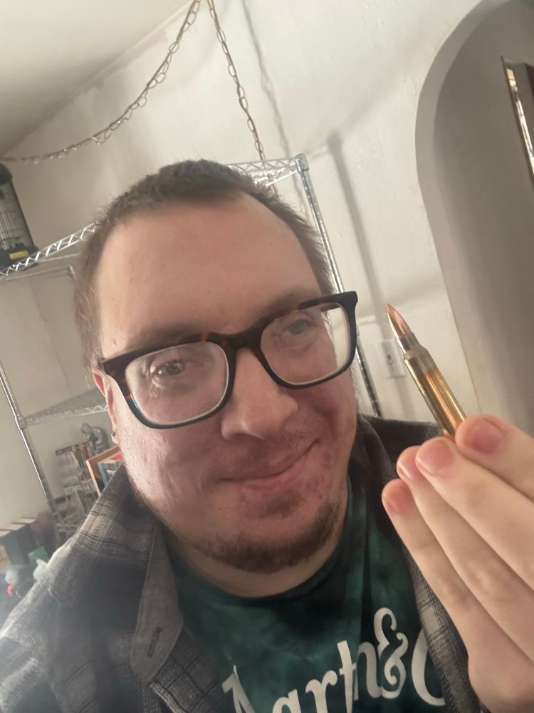 Madeline trans woman with short hair and glasses holding a large bullet 