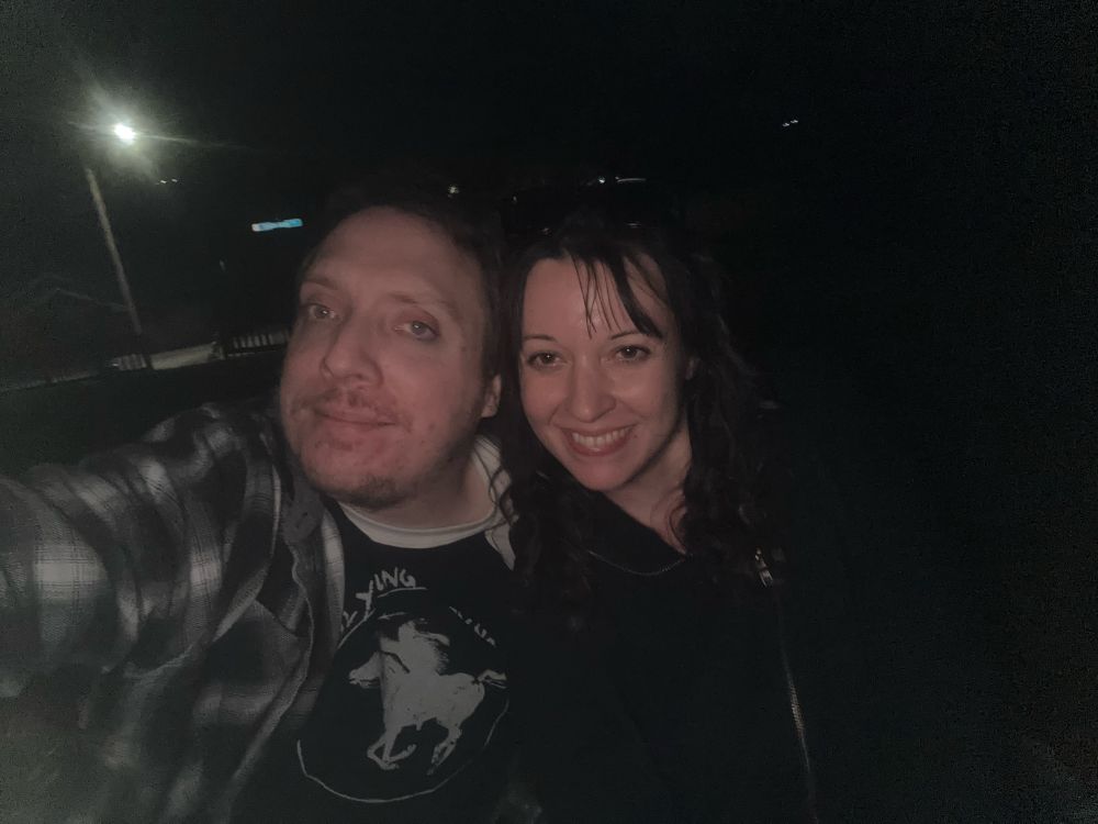 Two people one masculine with short hair and one feminine with mid length black hair no hair standing in front of a street light 