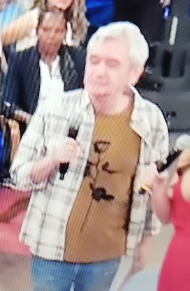 O apresentador Serginho Groisman, no programa "Altas Horas" da TV Globo, na noite do Sábado 14/06/2025.

Ele está usando uma calça jeans azul, uma camiseta amarela escuro (quase marrom) com o desenho de uma flor pintada de preto. Por cima desta camiseta, ele está usando uma camisa de flanela quadriculada, branca com listras cinzas.