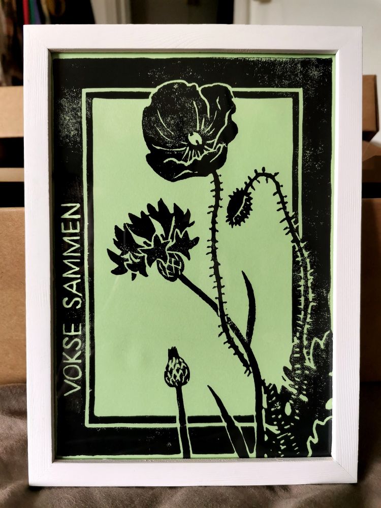 linocut print of cornflower and common poppy entangled. text on the side reads vokse sammen. danish for to grow together.