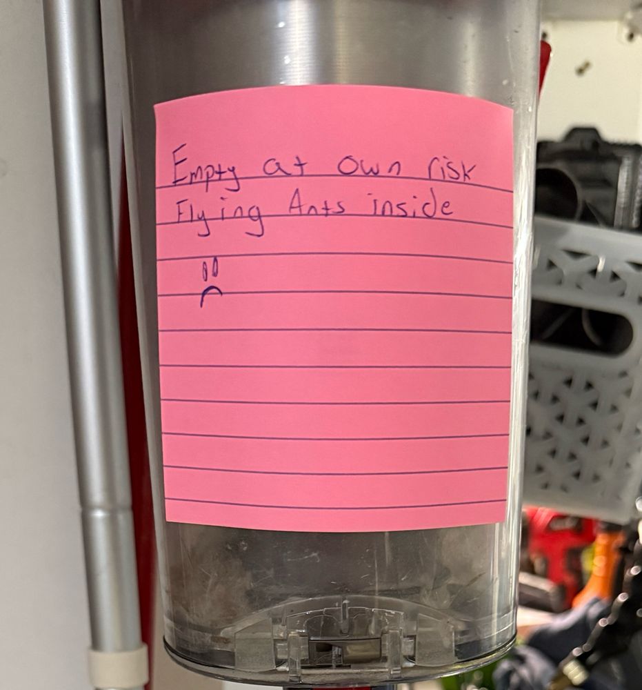 A vacuum canister with a sticky note that reads “empty at own risk. Flying Ants Inside
 :( “ 