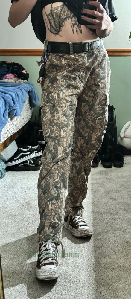 Danni is wearing camo cargo pants paired with brown platform coverse. Their shoes are muddied up and in desperate need of a lick. 