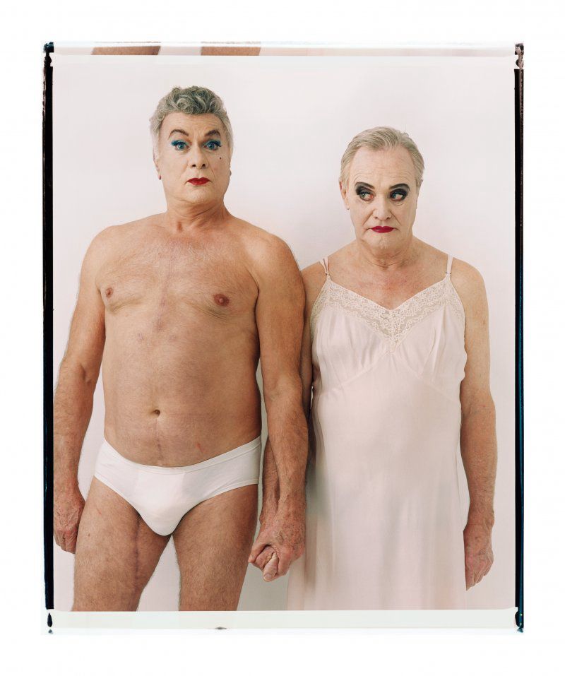 Two older men holding hands. One wearing just white y-fronts, the other in a pink chemis. Both are wearing eye shadow and lipstick. Tony Curtis and Jack Lemmon
