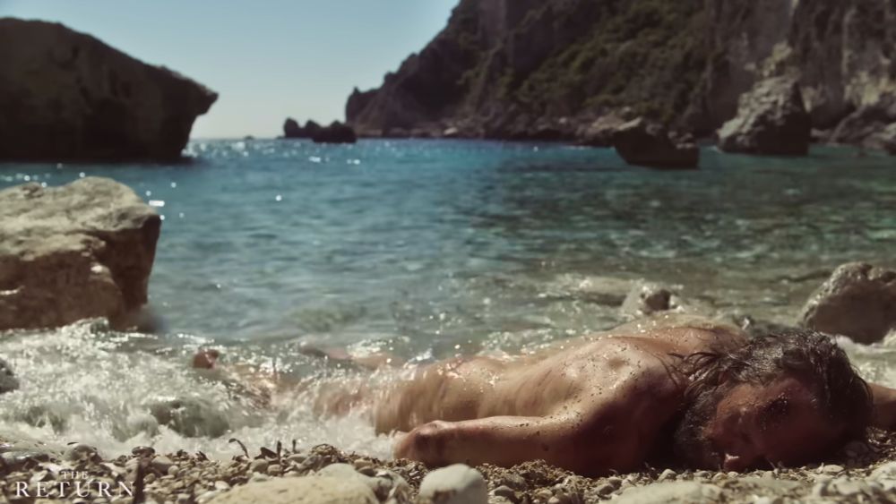 Naked man washed up on a mediterranean pebbled beach blasted by the Sun.