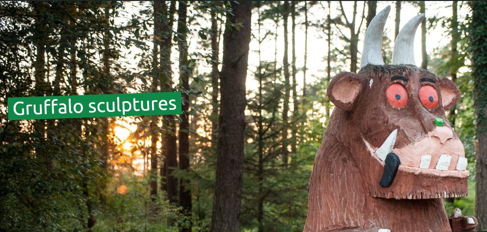 Forest photo with wooden sculpture of a Gruffalo, big brown with large horns. Type on photo says 