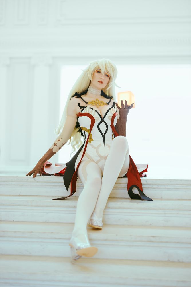 A cosplay of Asmoday from Genshin impact. She's seated on a white marble staircase and holding a glowing golden cube in one hand. Behind her, the background is bathed in bright white light.