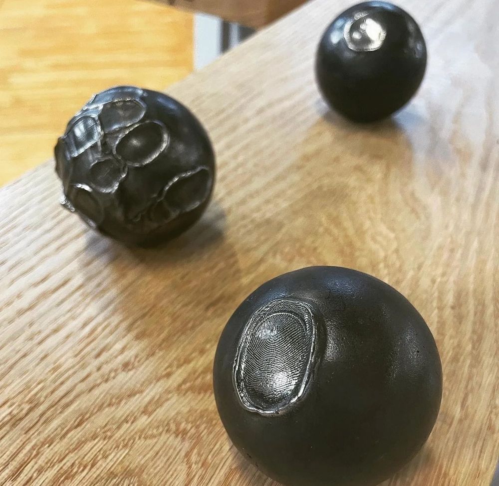 Image: photo of three balls of – probably – cast iron; each is black and has an impress on its surface; on one the impression seems to include a fingerprint, on another, maybe something to do with the bones of the hand • “The Score is a multifaceted contemporary art project by Cork-based artist James L Hayes, developed in collaboration with and curated by composer Peter Power, combining cast iron sculpture, film, and sound. The work explores the materiality, heritage, and cultural spectacle of the ancient Irish sport of road bowling.    GOMA Gallery of Modern Art in Waterford City is thrilled to announce the launch of The Score & Other Works by James L Hayes.    The Score is a multifaceted contemporary art project by Cork-based artist James L Hayes, developed in collaboration with and curated by Peter Power, combining cast iron sculpture, film, and sound. The work explores the materiality, heritage, and cultural spectacle of the ancient Irish sport of road bowling…”