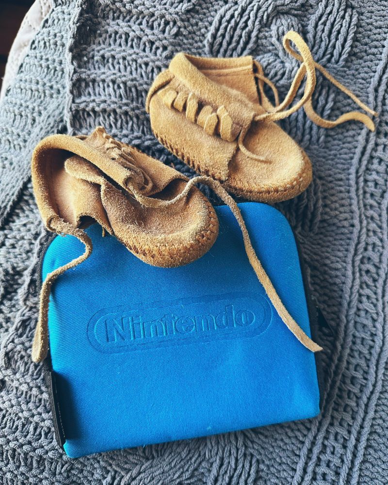 A Nintendo 2DS in a blue case along with little moccasins when I was baby. 