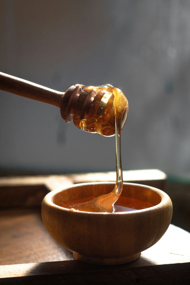 A wooden honey dipper with honey flowing into a wooden bowl